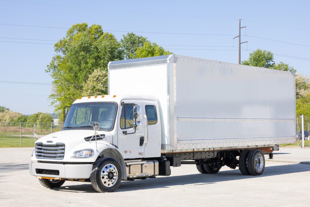 A white commercial truck is parked on an asphalt surface under a clear sky.