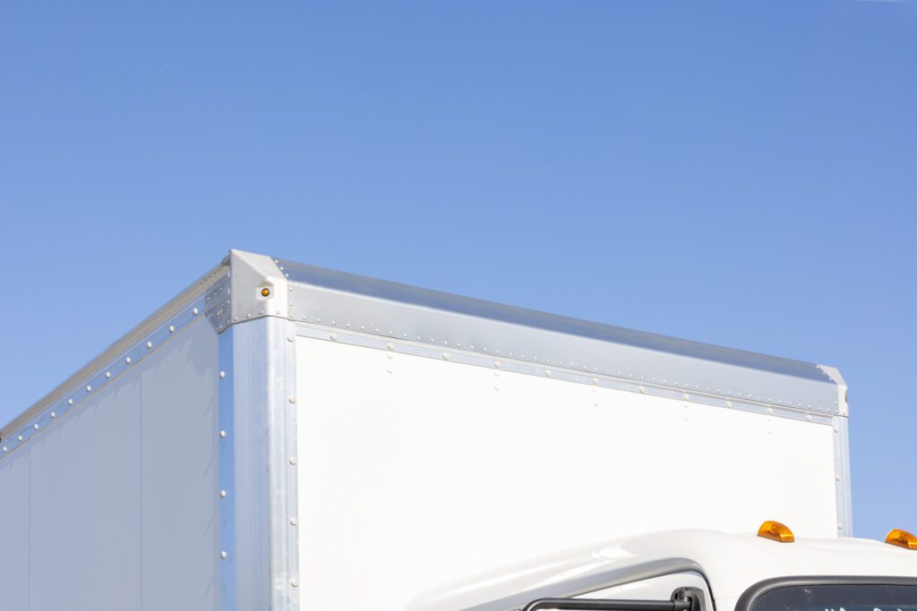 A white delivery truck is parked under a clear blue sky.